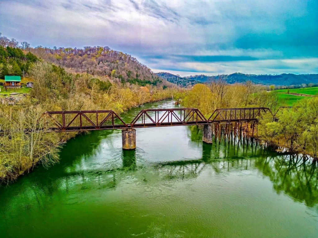 Scenic river flowing beneath a historic railroad bridge surrounded by mountains in the Tennessee Valley, representing communities served by Team Morris Homes.