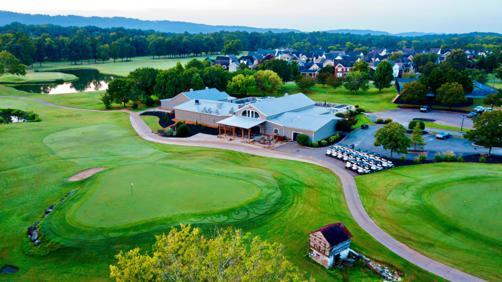 Aerial view of The Ooltewah Club golf course and clubhouse in Ooltewah, Tennessee, featuring manicured greens, a pond, and surrounding homes.